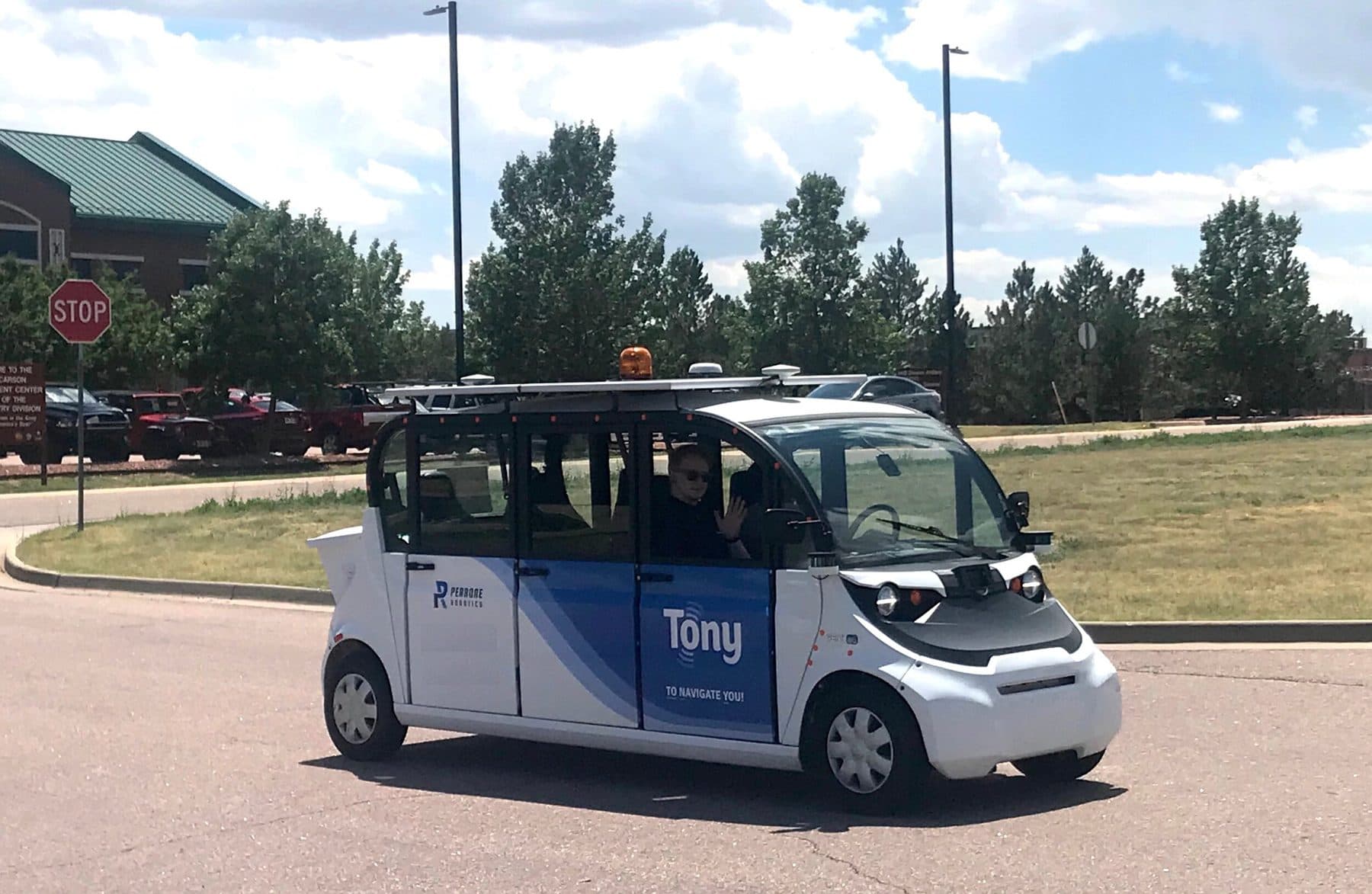 Automated shuttle named Tony driving on a road at Fort Carson with a passenger waving